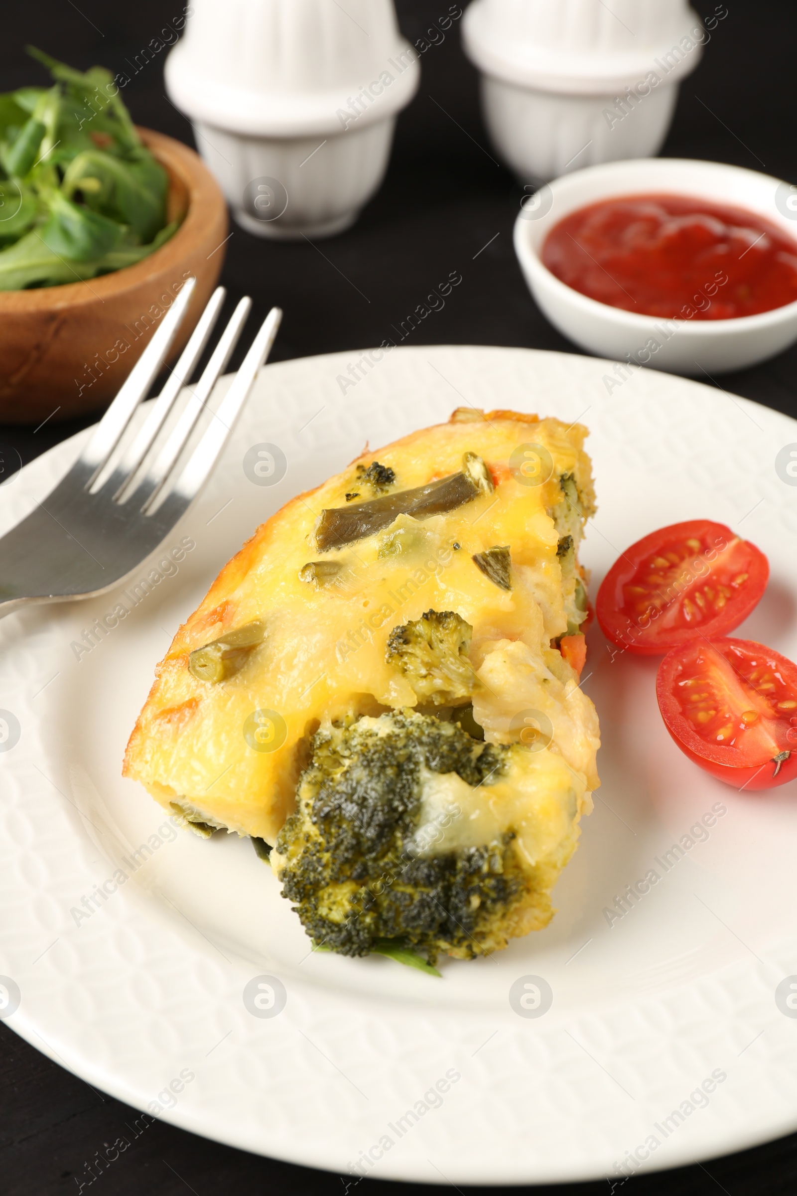 Photo of Tasty vegetable casserole and tomato on black table, closeup