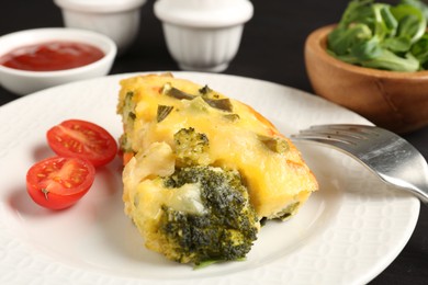 Photo of Tasty vegetable casserole and tomato on black table, closeup