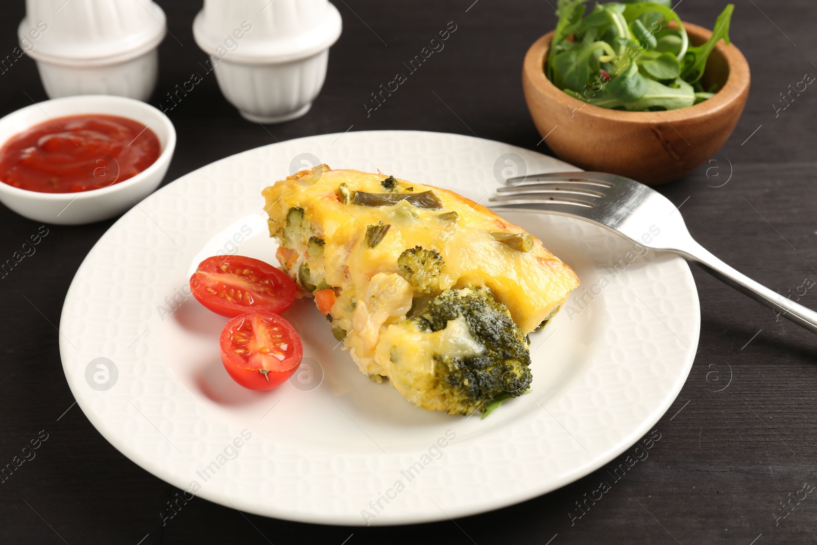 Photo of Tasty vegetable casserole and tomato on black wooden table, closeup