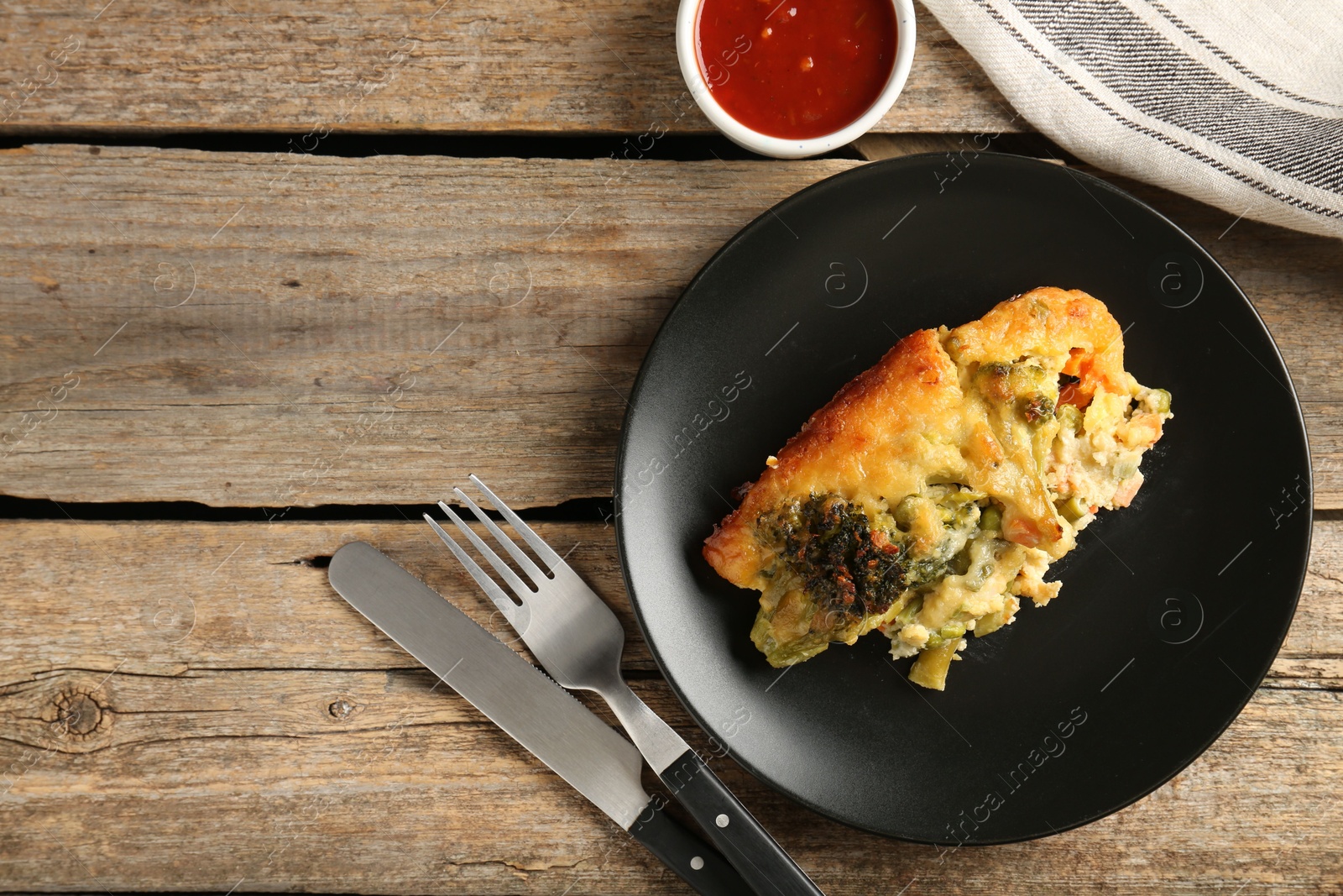 Photo of Tasty vegetable casserole, sauce and cutlery on wooden table, flat lay. Space for text