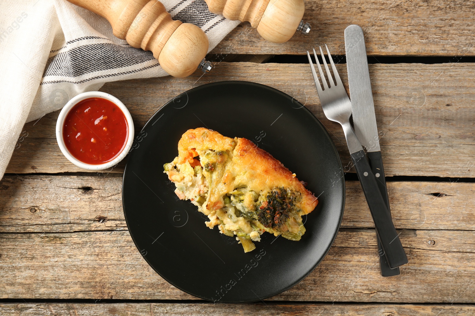 Photo of Tasty vegetable casserole, sauce, cutlery and shakers on wooden table, flat lay