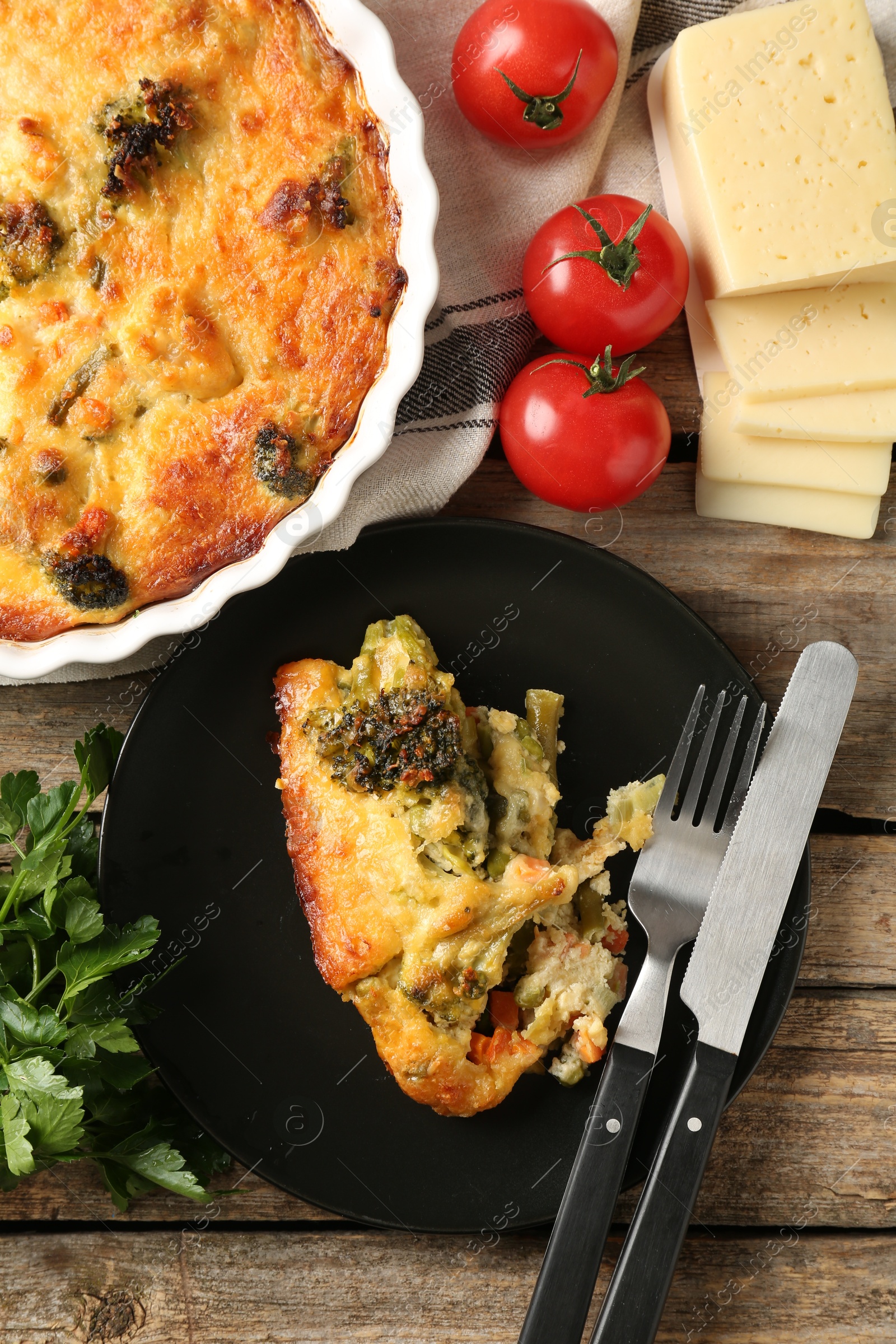 Photo of Tasty vegetable casserole, products and cutlery on wooden table, flat lay