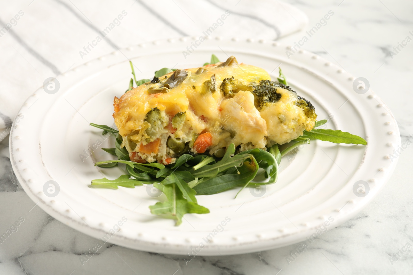 Photo of Tasty vegetable casserole and arugula on white marble table, closeup