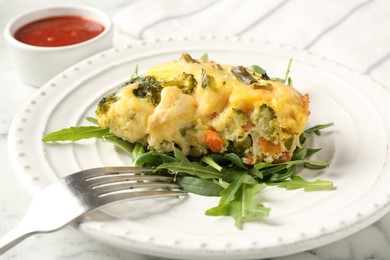 Photo of Tasty vegetable casserole, arugula and fork on white marble table, closeup