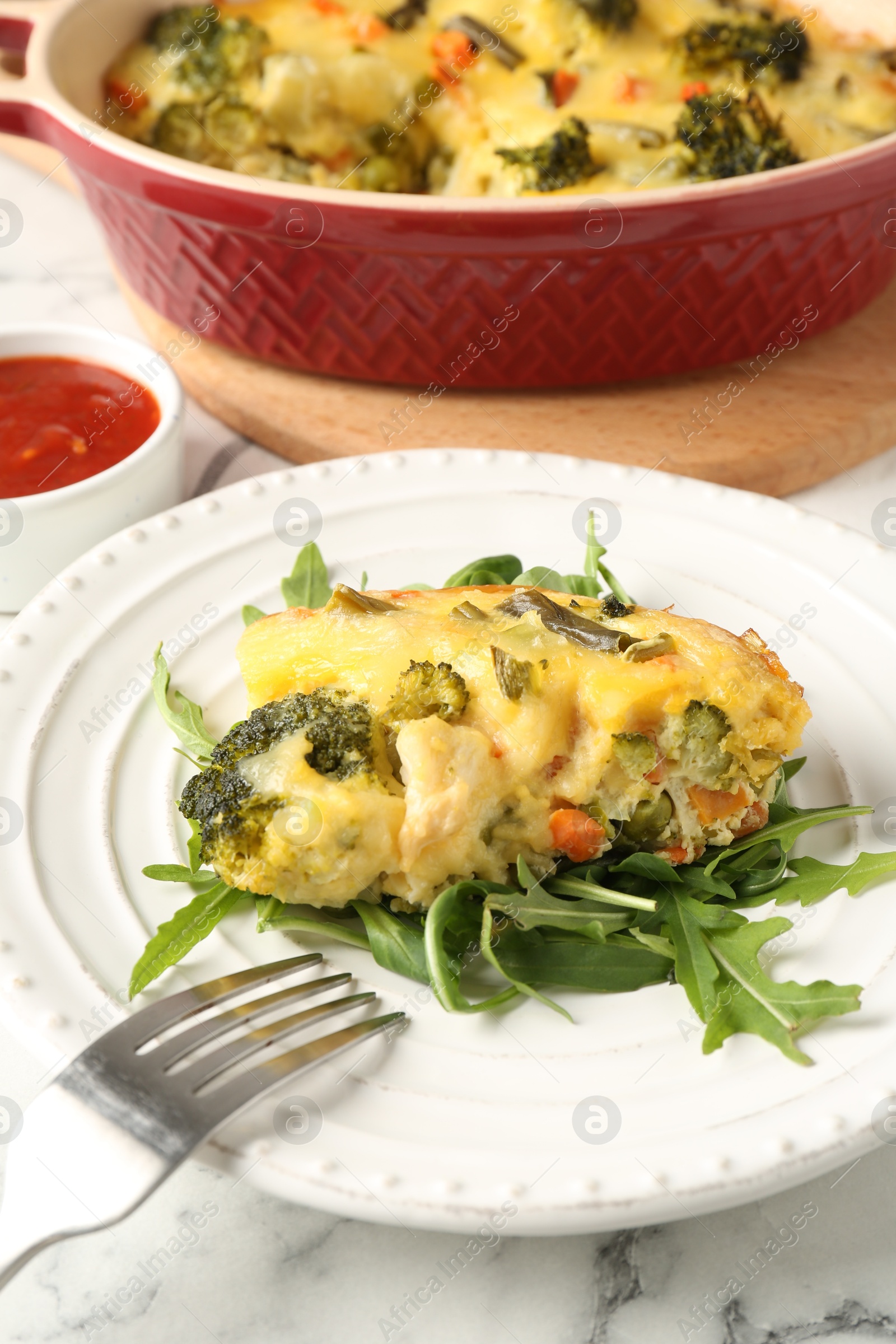 Photo of Tasty vegetable casserole, arugula and fork on white marble table, closeup