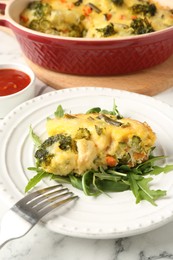 Photo of Tasty vegetable casserole, arugula and fork on white marble table, closeup