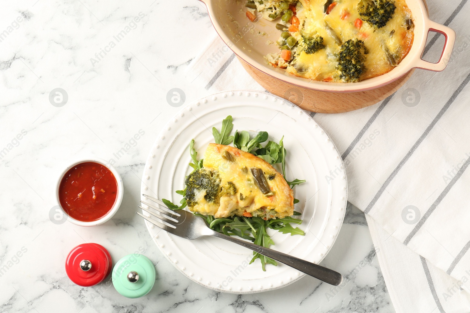 Photo of Tasty vegetable casserole, arugula, shakers, sauce and fork on white marble table, flat lay