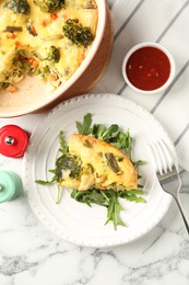 Photo of Tasty vegetable casserole, arugula, shakers, sauce and fork on white marble table, flat lay