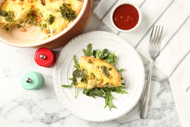 Photo of Tasty vegetable casserole, arugula, shakers, sauce and fork on white marble table, flat lay