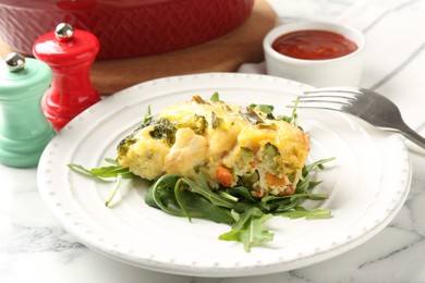 Photo of Tasty vegetable casserole, arugula and fork on white marble table, closeup