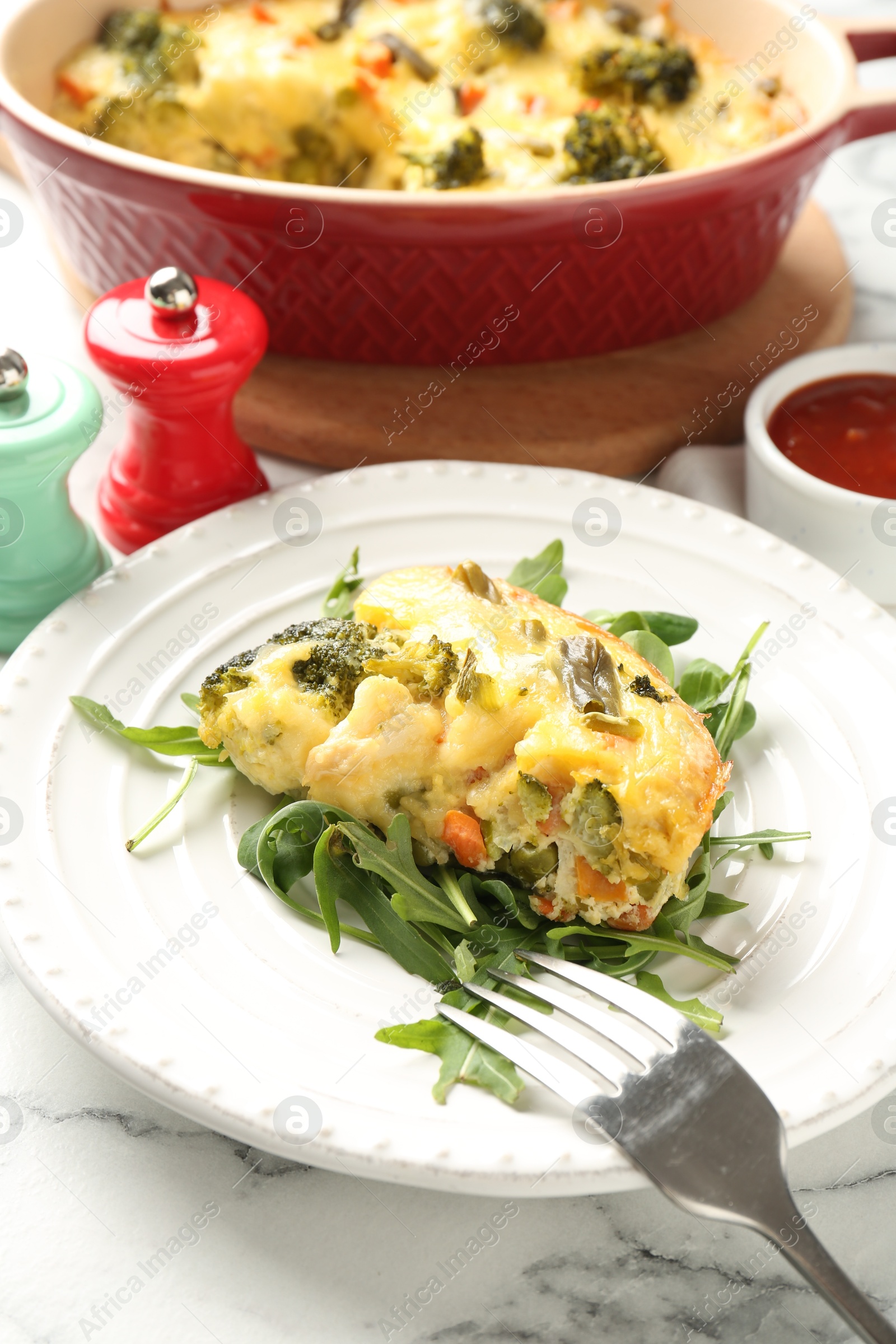 Photo of Tasty vegetable casserole, arugula and fork on white marble table, closeup