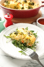 Photo of Tasty vegetable casserole, arugula and fork on white marble table, closeup