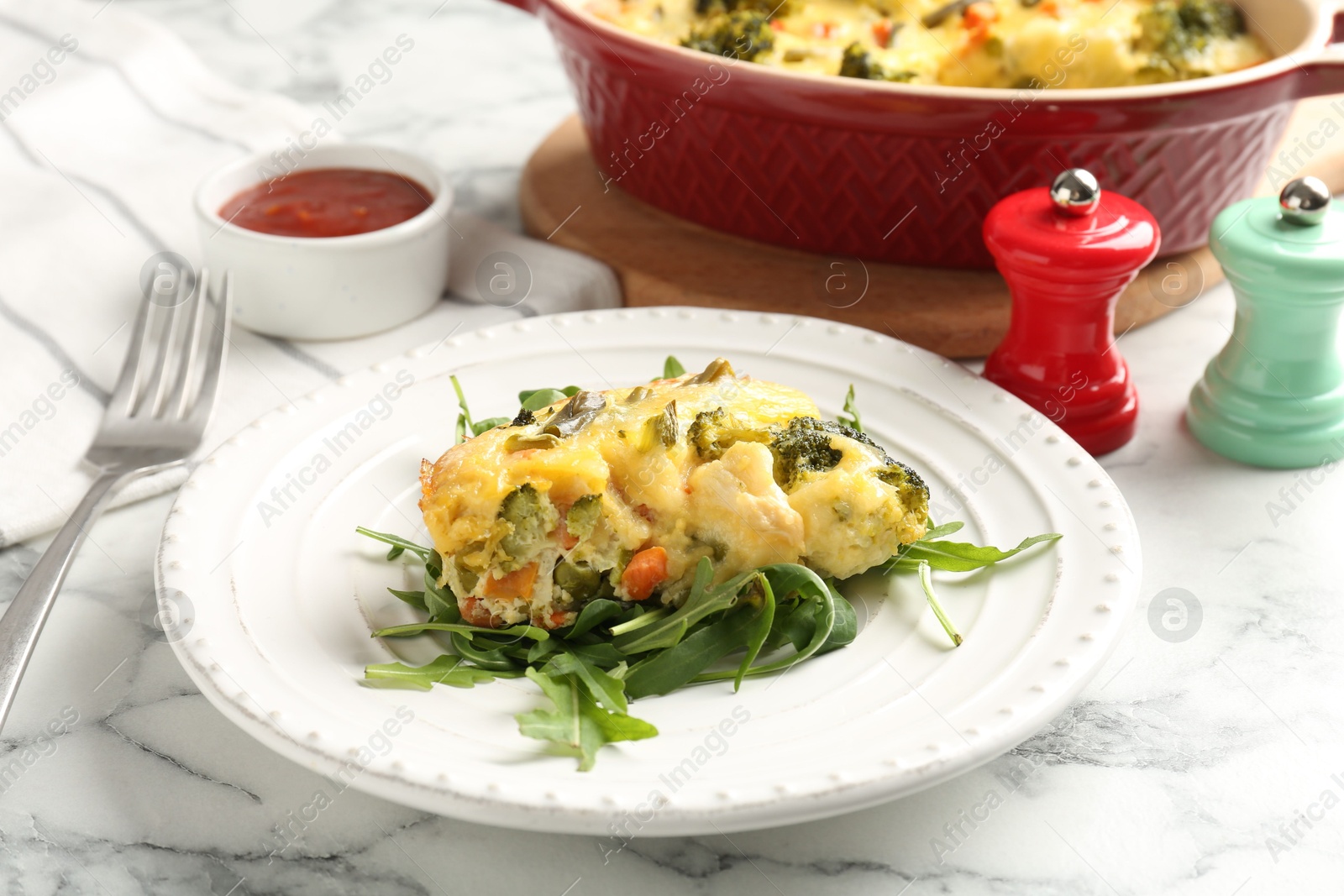 Photo of Tasty vegetable casserole and arugula on white marble table, closeup