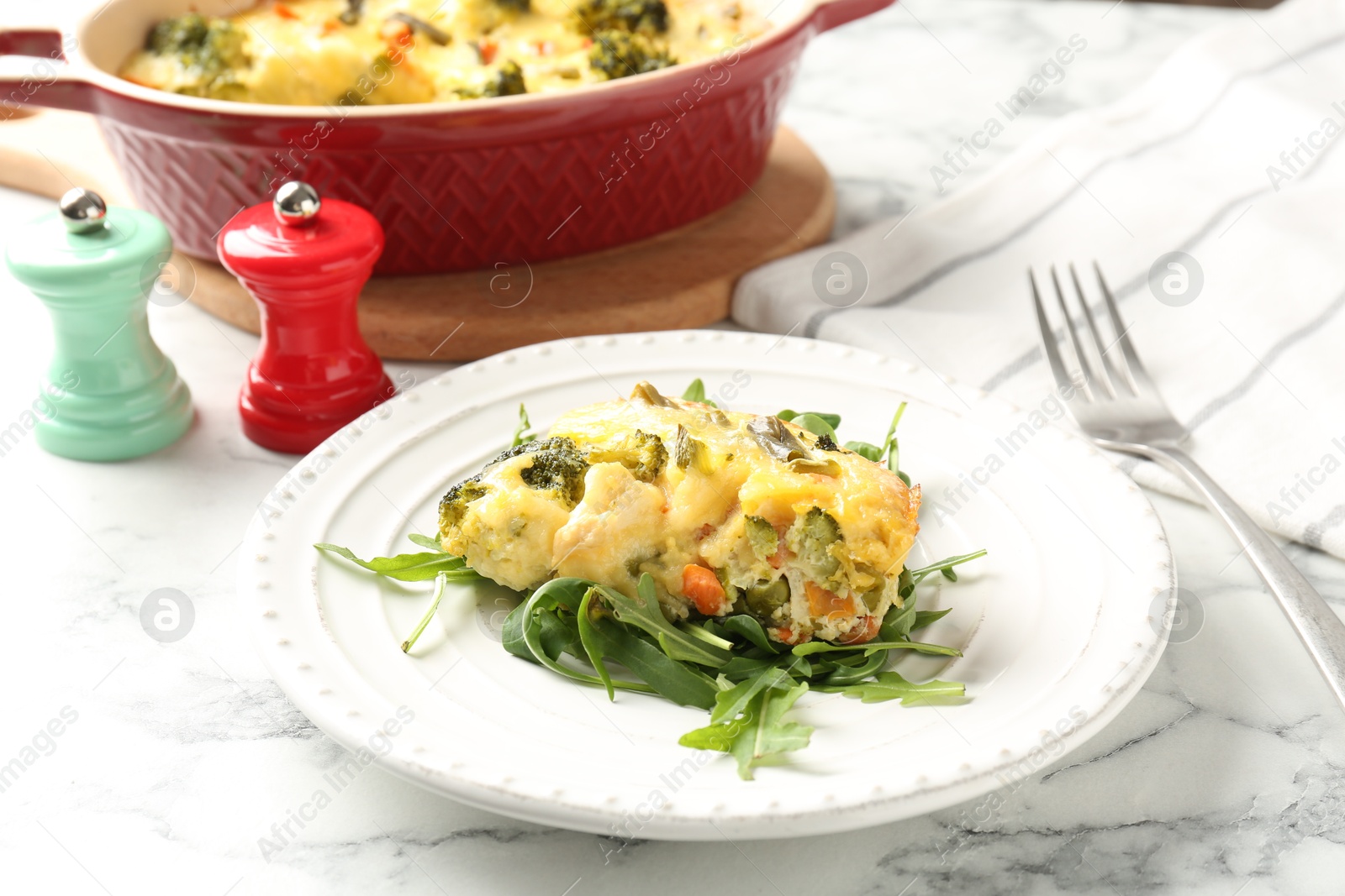 Photo of Tasty vegetable casserole and arugula on white marble table, closeup