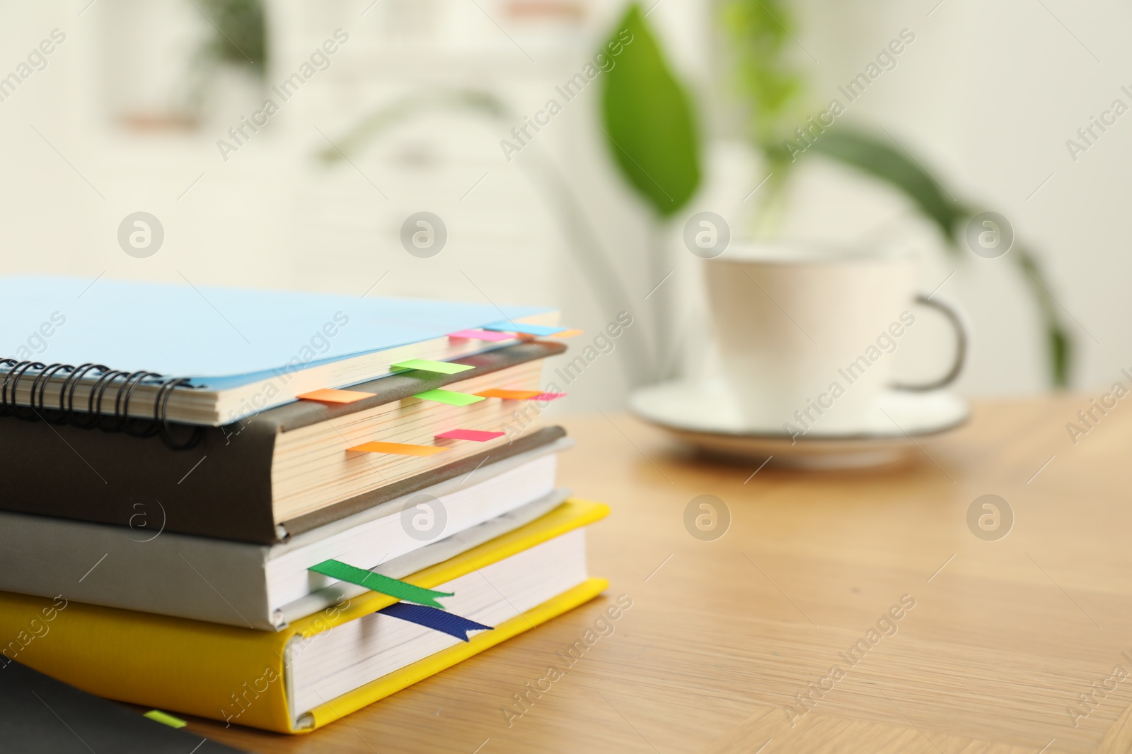 Photo of Stack of books and notebook with colorful bookmarks on wooden table, closeup. Space for text