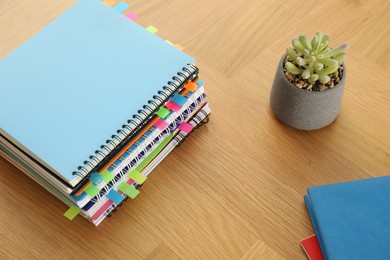 Photo of Stack of notebooks with colorful bookmarks and houseplant on wooden table, above view