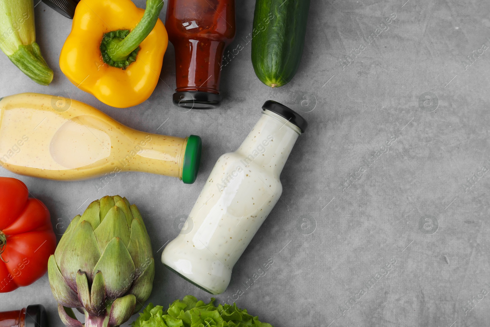 Photo of Tasty sauces in glass bottles and fresh products on light grey table, flat lay. Space for text