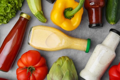 Photo of Tasty sauces in glass bottles and fresh products on light grey table, flat lay