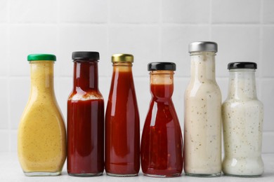 Photo of Tasty sauces in glass bottles on white table, closeup