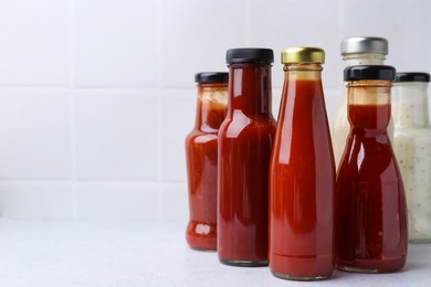 Photo of Tasty sauces in glass bottles on white table, closeup. Space for text