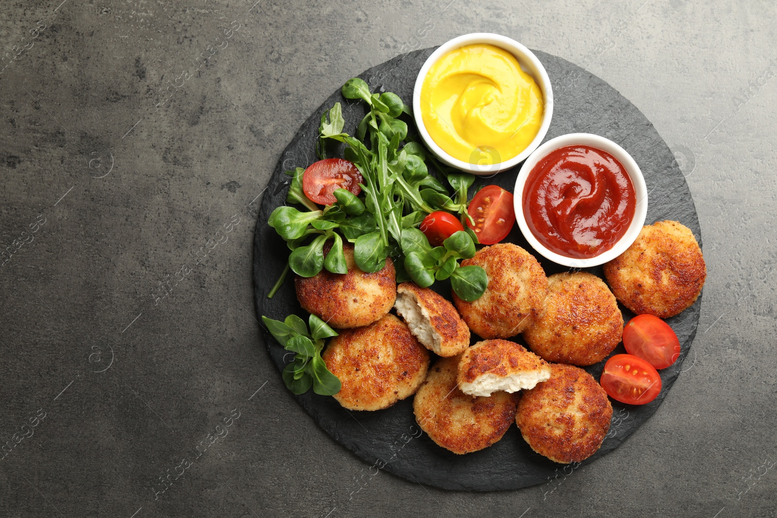 Tasty patties, tomato, spinach, mustard and ketchup on grey textured table, top view. Space for text Photo of Tasty patties, tomato, spinach, mustard and ketchup on grey textured table, top view. Space for text