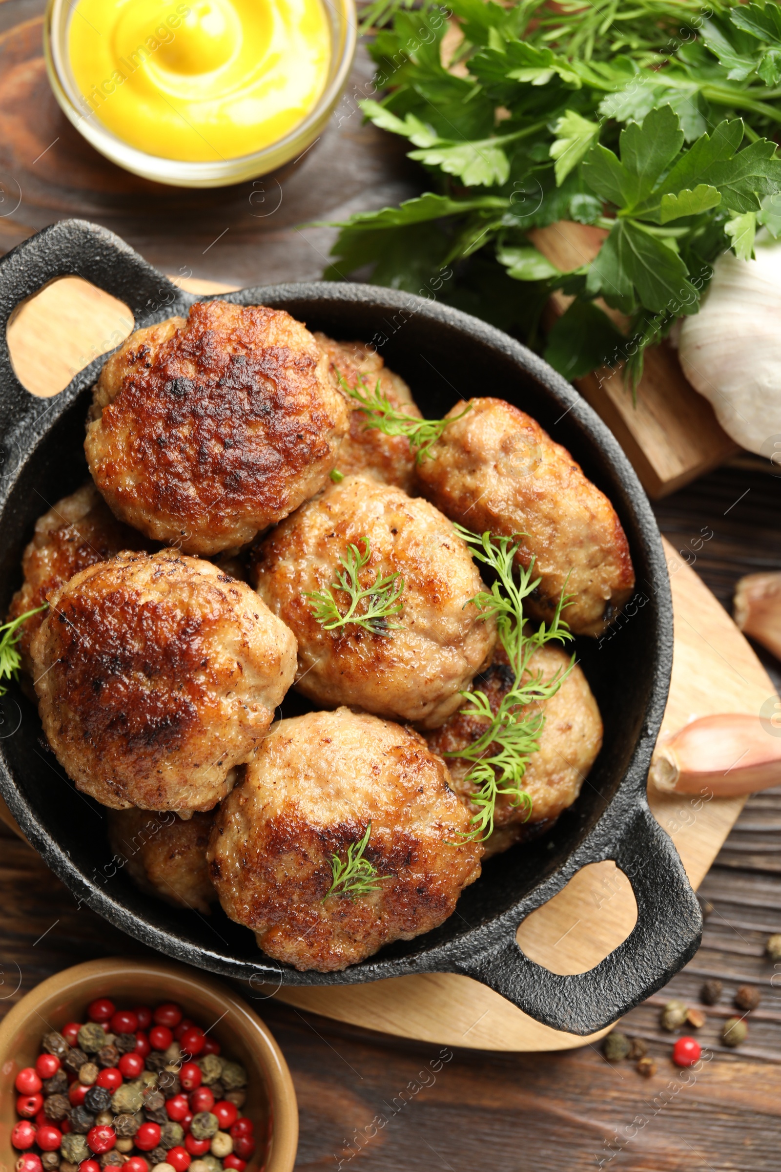 Photo of Tasty patties, dill in frying pan, parsley, mustard and peppercorns on wooden table, flat lay