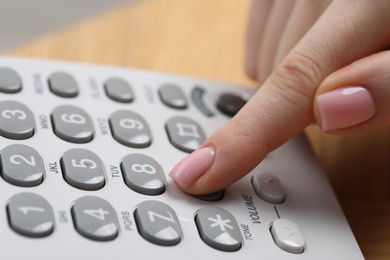 Photo of Woman dialing number on telephone against blurred background, closeup