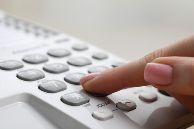 Photo of Woman dialing number on telephone against blurred grey background, closeup