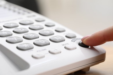 Photo of Woman dialing number on telephone against blurred grey background, closeup