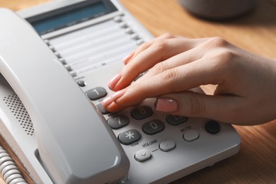 Photo of Woman dialing number on telephone at wooden table, closeup