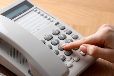 Photo of Woman dialing number on telephone at wooden table, closeup