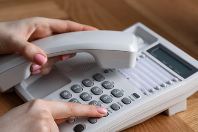 Photo of Woman dialing number on telephone at wooden table, closeup