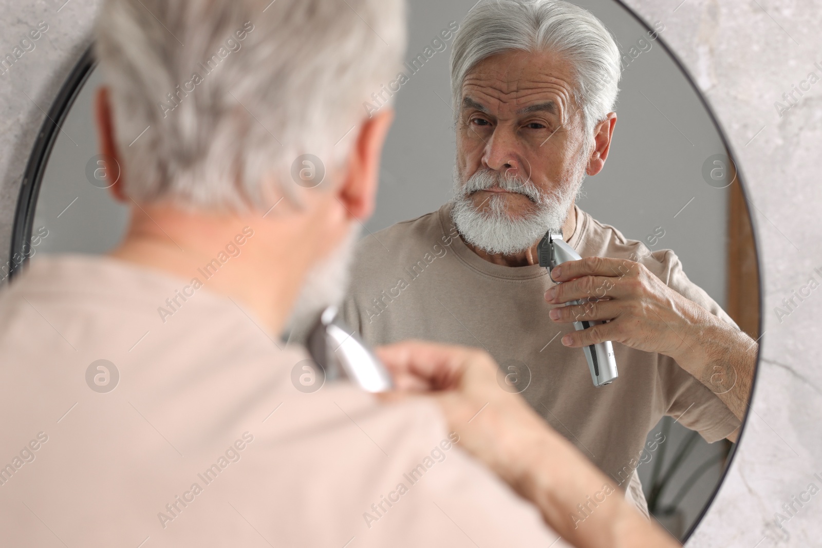 Photo of Senior man trimming beard near mirror in bathroom