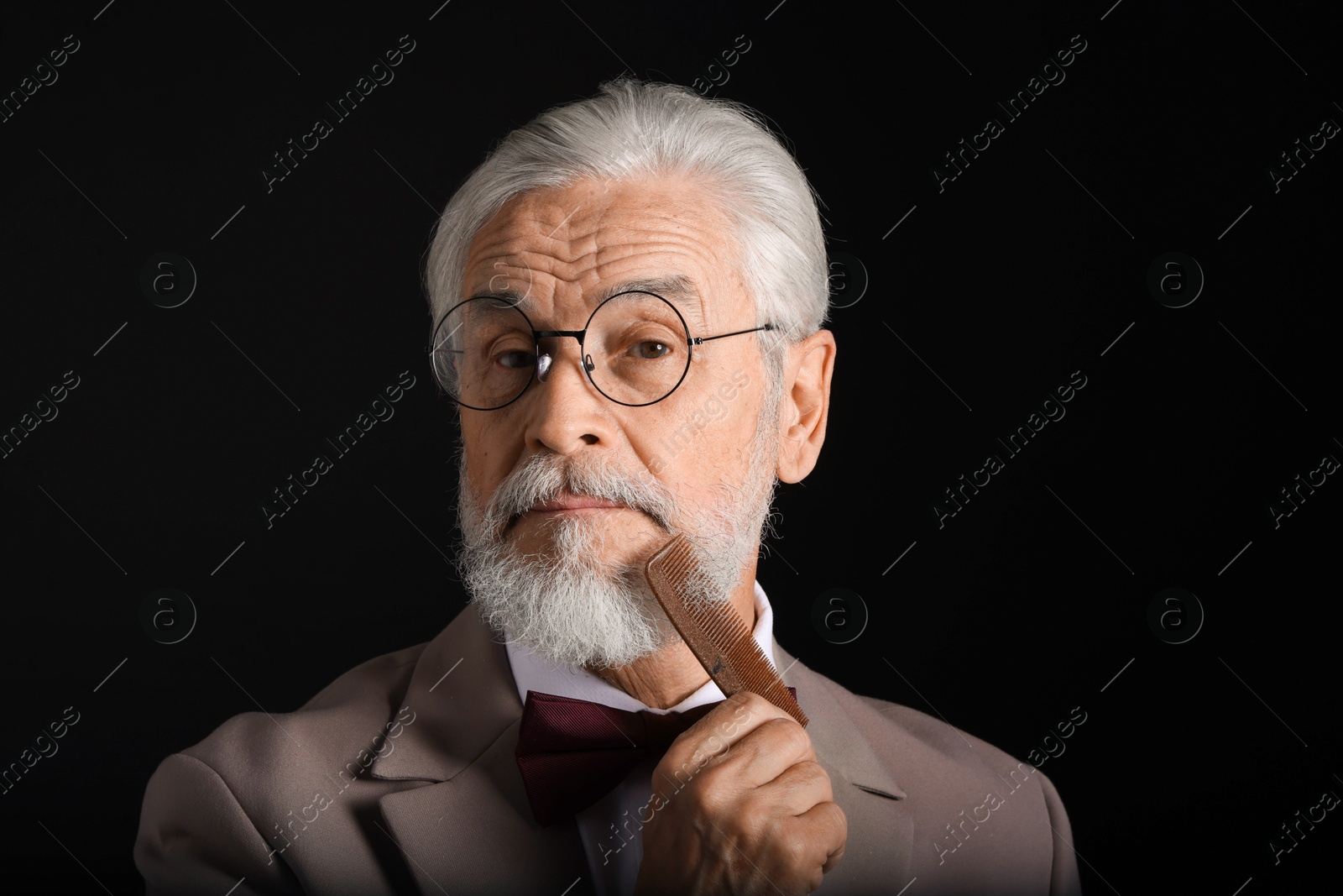 Photo of Senior man combing beard on black background