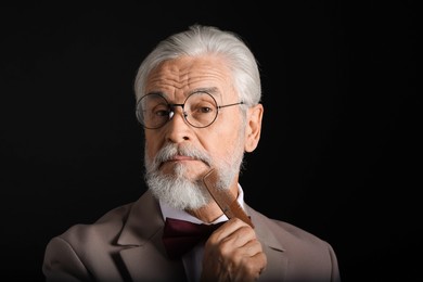 Photo of Senior man combing beard on black background