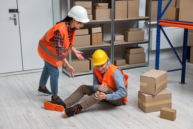 Photo of Accident at work. Woman helping her injured colleague in warehouse