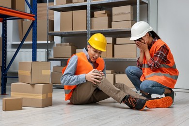 Photo of Accident at work. Woman helping her injured colleague in warehouse