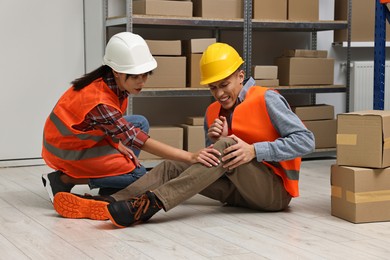 Photo of Accident at work. Woman helping her injured colleague in warehouse