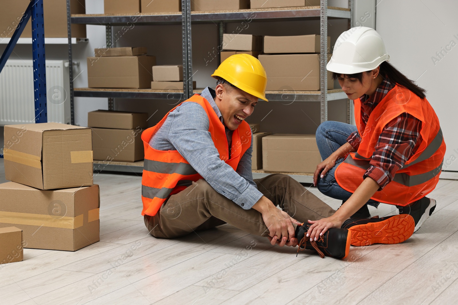 Photo of Accident at work. Woman helping her injured colleague in warehouse