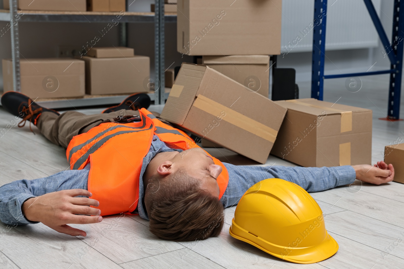 Photo of Accident at work. Unconscious man lying on floor in warehouse