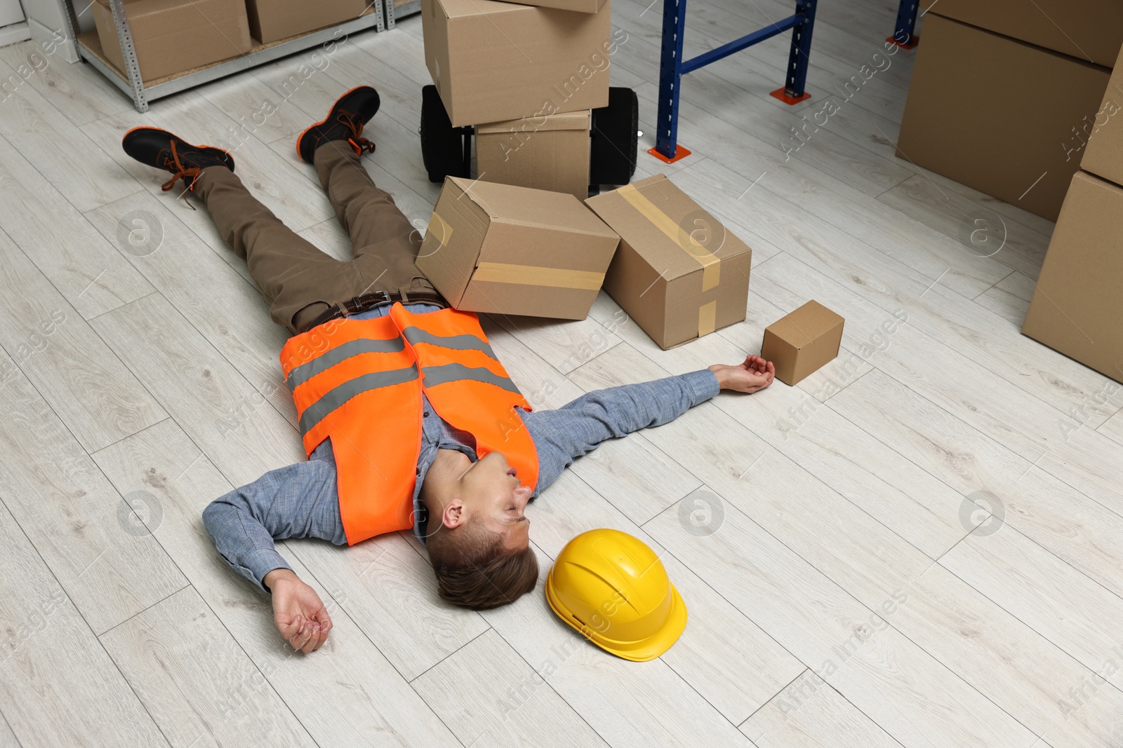 Photo of Accident at work. Unconscious man lying on floor in warehouse