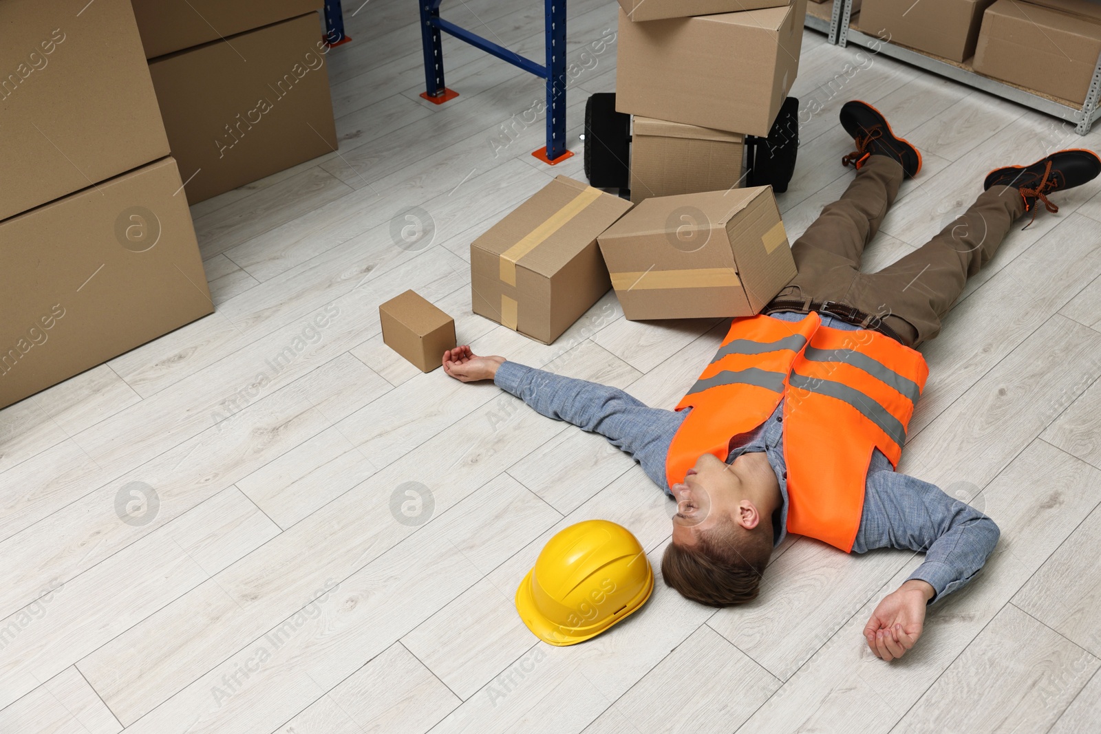 Photo of Accident at work. Unconscious man lying on floor in warehouse. Space for text