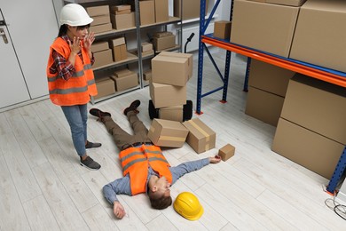 Photo of Accident at work. Worried woman and her unconscious colleague in warehouse