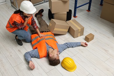 Photo of Accident at work. Worried woman and her unconscious colleague in warehouse