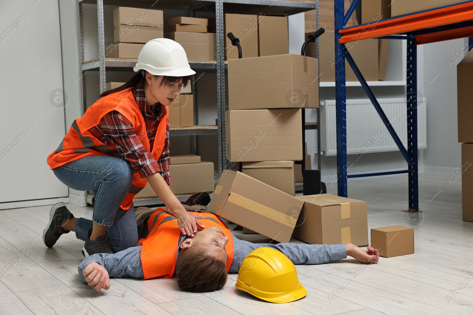 Photo of Accident at work. Woman checking pulse of her unconscious colleague in warehouse