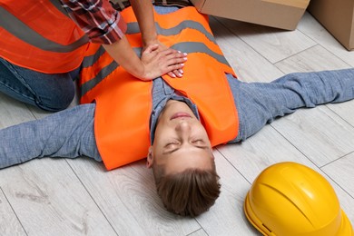 Photo of Accident at work. Woman performing CPR on her unconscious colleague in warehouse, closeup