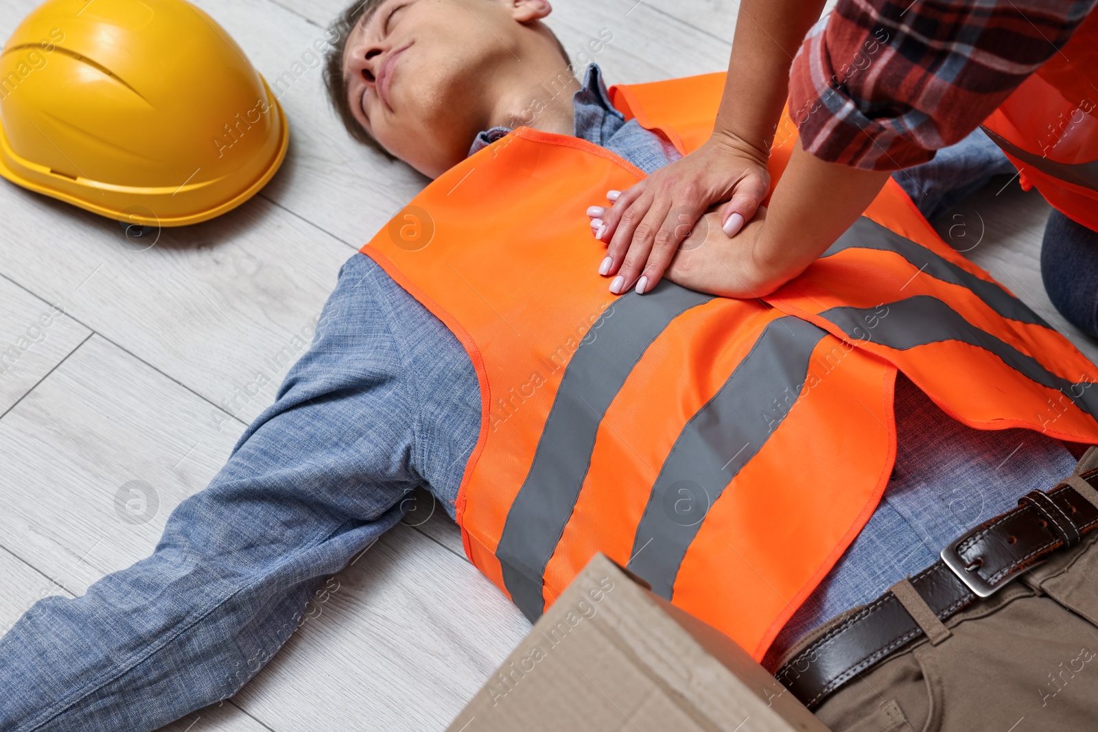 Photo of Accident at work. Woman performing CPR on her unconscious colleague in warehouse, closeup