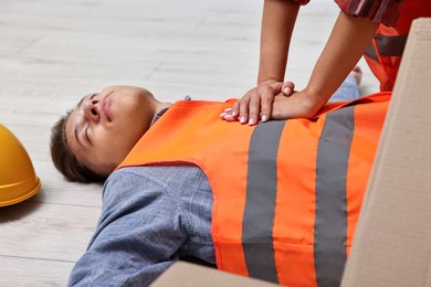 Accident at work. Woman performing CPR on her unconscious colleague in warehouse, closeup