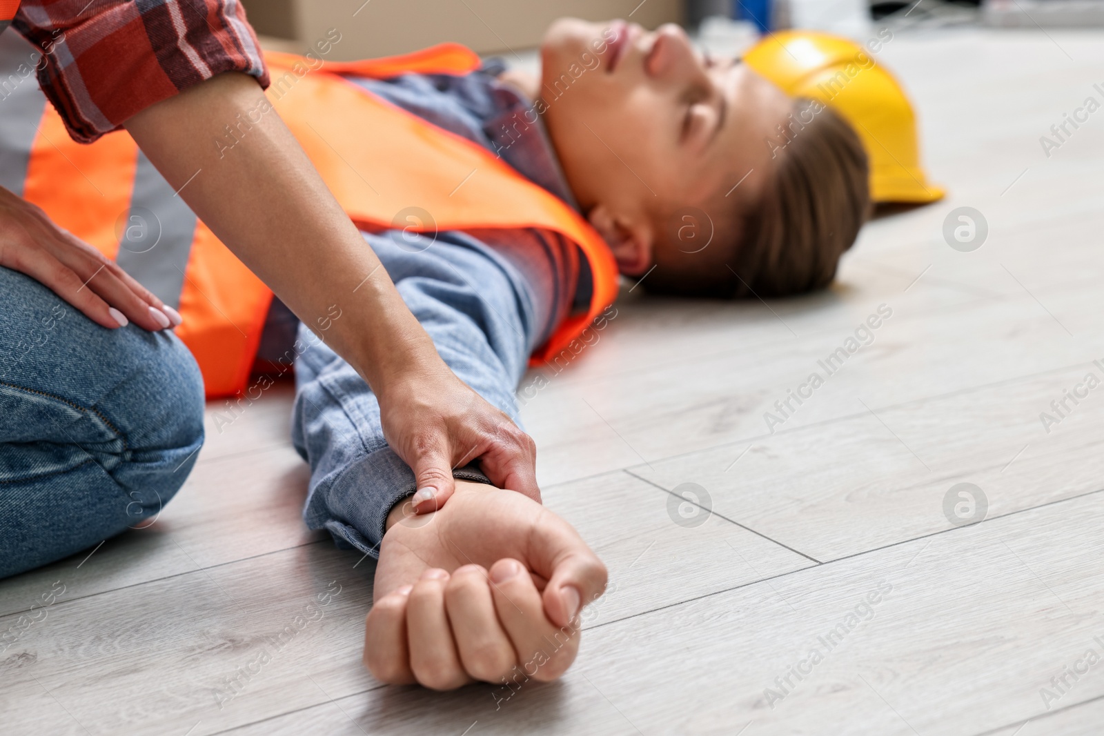 Photo of Accident at work. Woman checking pulse of his unconscious colleague in warehouse, closeup