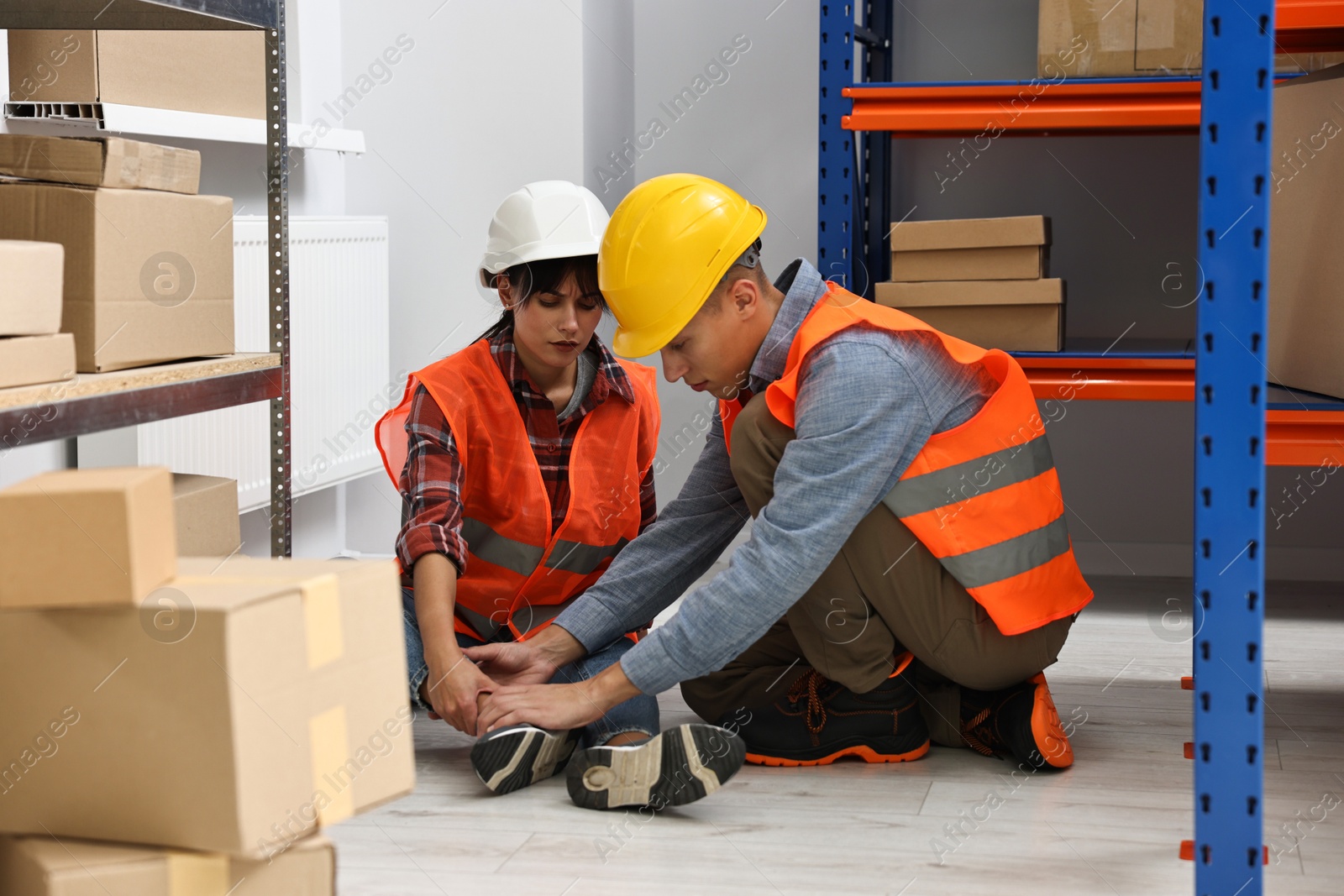 Photo of Accident at work. Man helping his injured colleague in warehouse